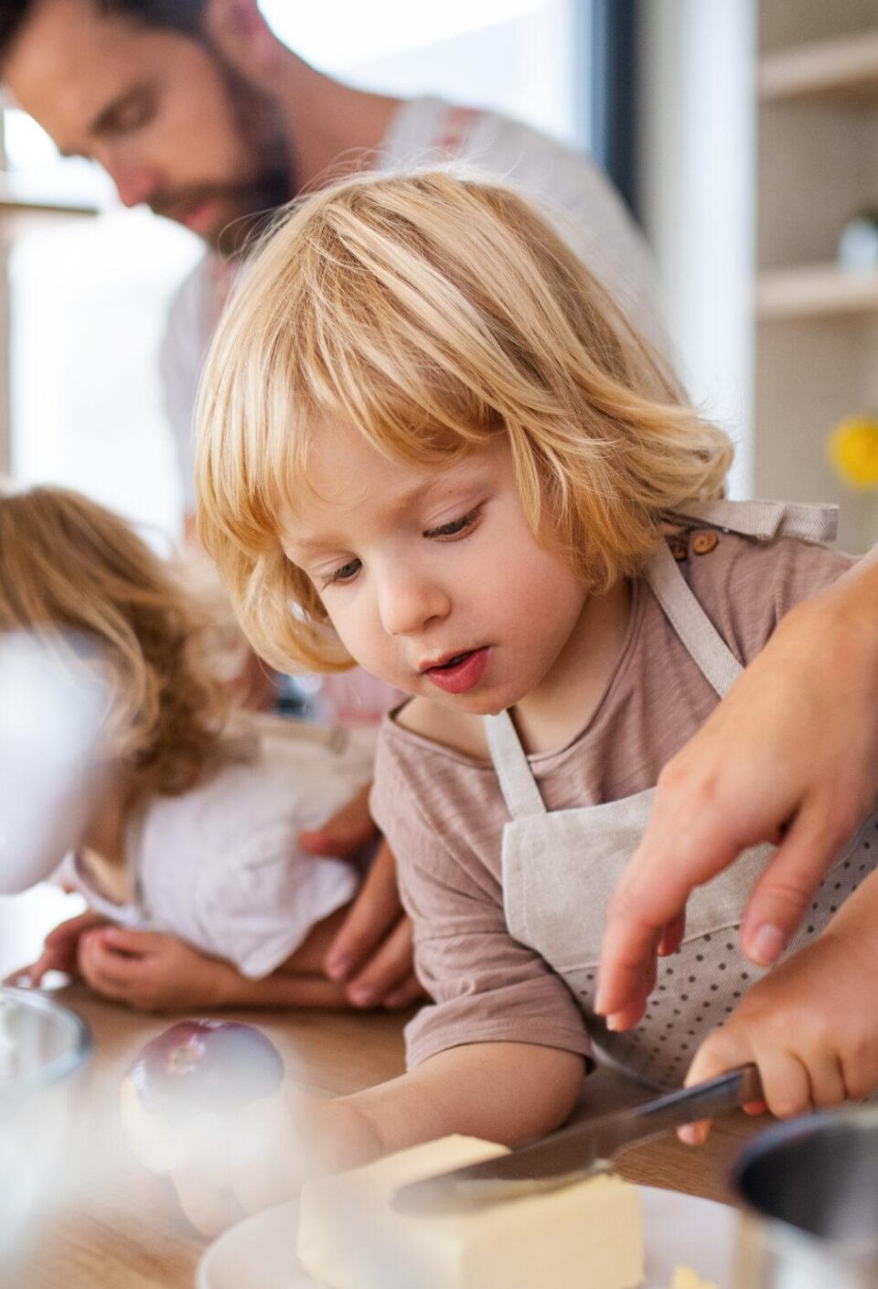 Young family with two small children indoors in kitchen, preparing food.