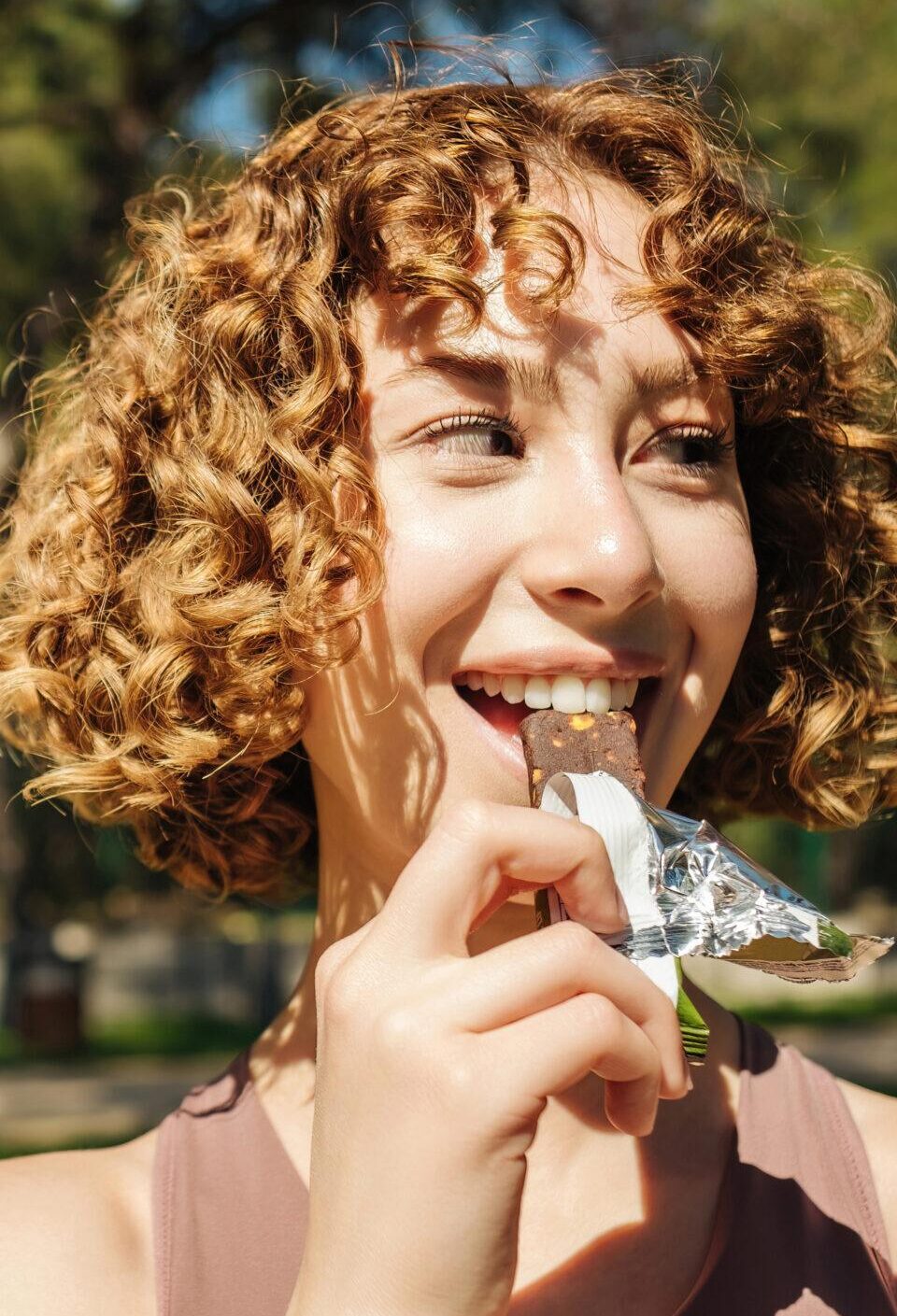 Athletic woman eating a protein bar. Fitness beautiful woman eating a energy snack outdoor. Copy space. Healthy food, outdoor sports concepts. Athletic woman eating a protein bar. Fitness beautiful woman eating a energy snack outdoor. Copy space. Healthy food, outdoor sports concepts.